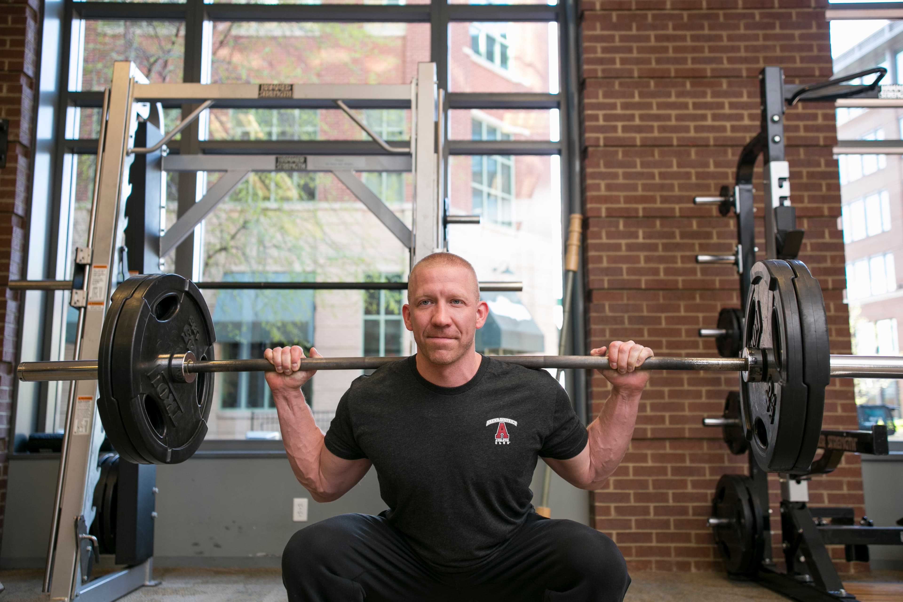 A member back squatting a loaded barbell in front of the brick wall