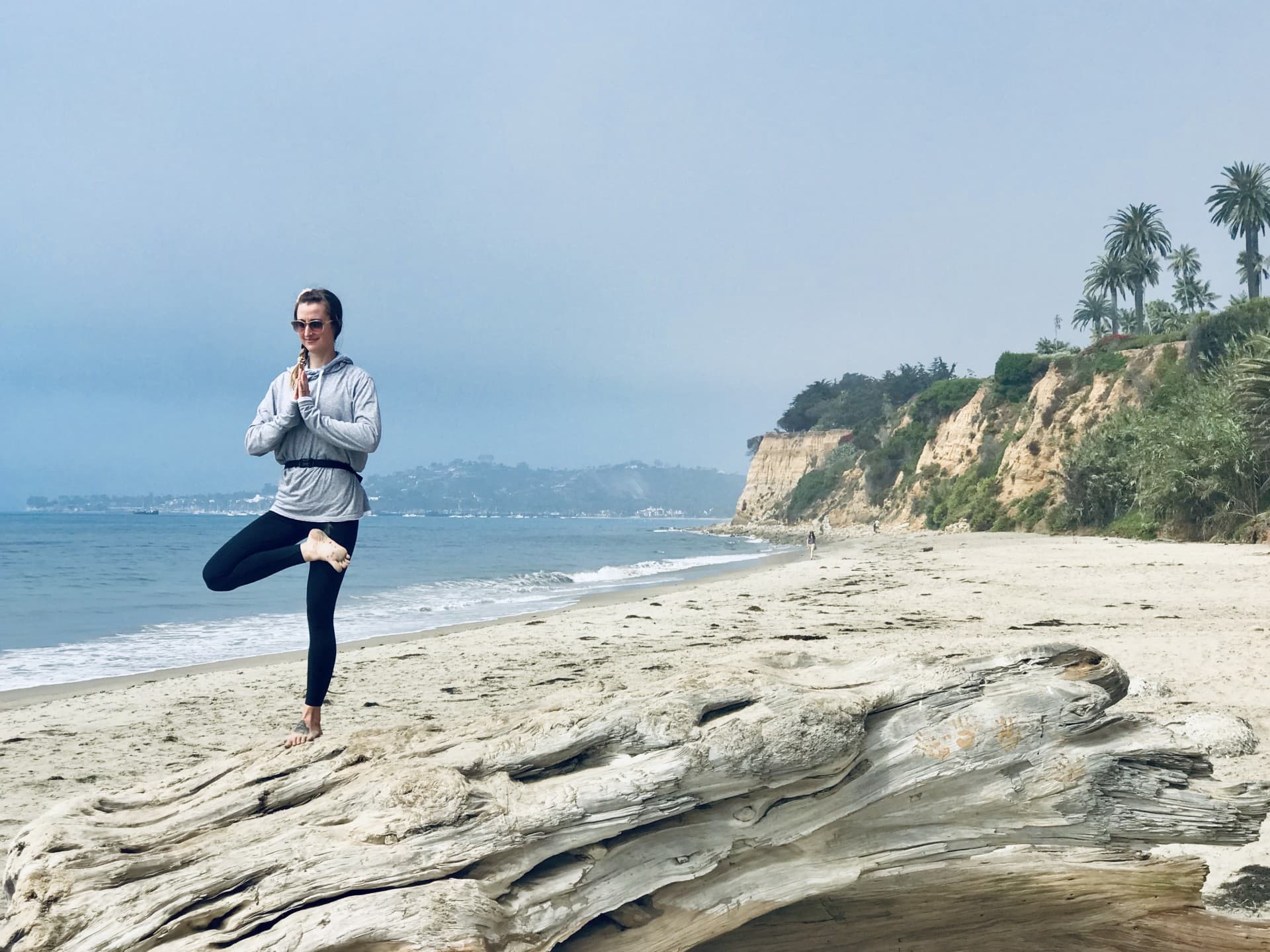 Maggie Fekete holding tree pose on a beach at the water's edge